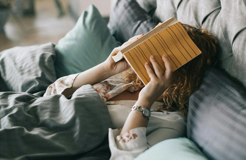 Woman laying in bed covering her face with a book.