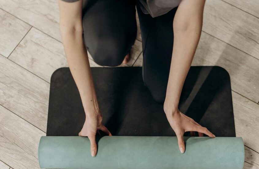 Woman in black leggings unrolling a yoga mat.