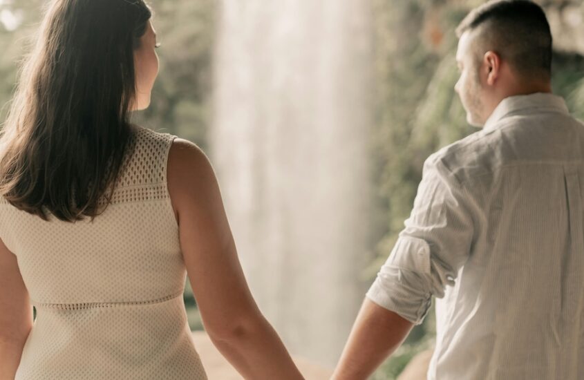 A woman and man holding hands in from of a waterfall.